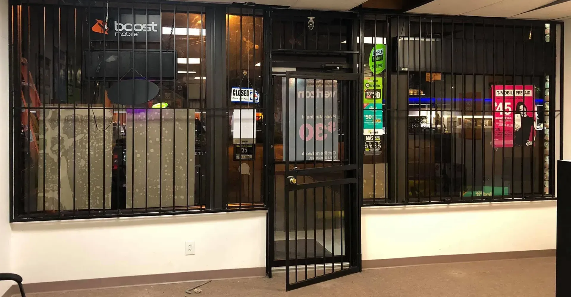 Closed storefront with barred windows and a central door, lit inside with neon signs at night