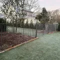 Fenced backyard with frosty grass, garden beds, and bare trees beside a house