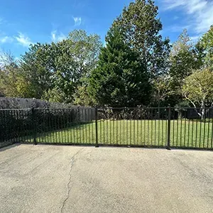 Black metal gate across a driveway with trees and blue sky behind it