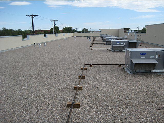 Flat rooftop with HVAC units and gravel surface under a clear sky