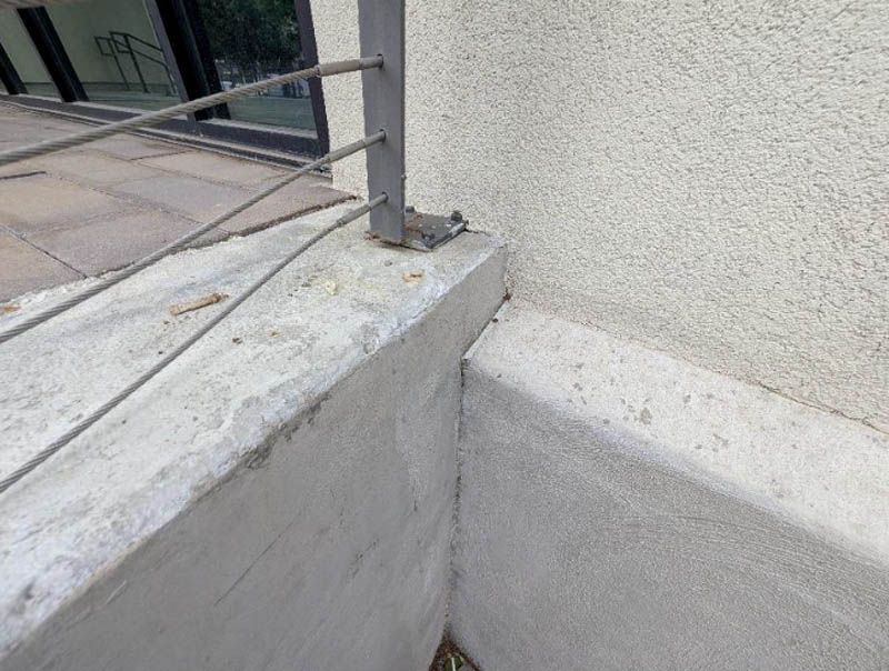 Concrete corner beside a metal railing with a visible crack at the base of a wall