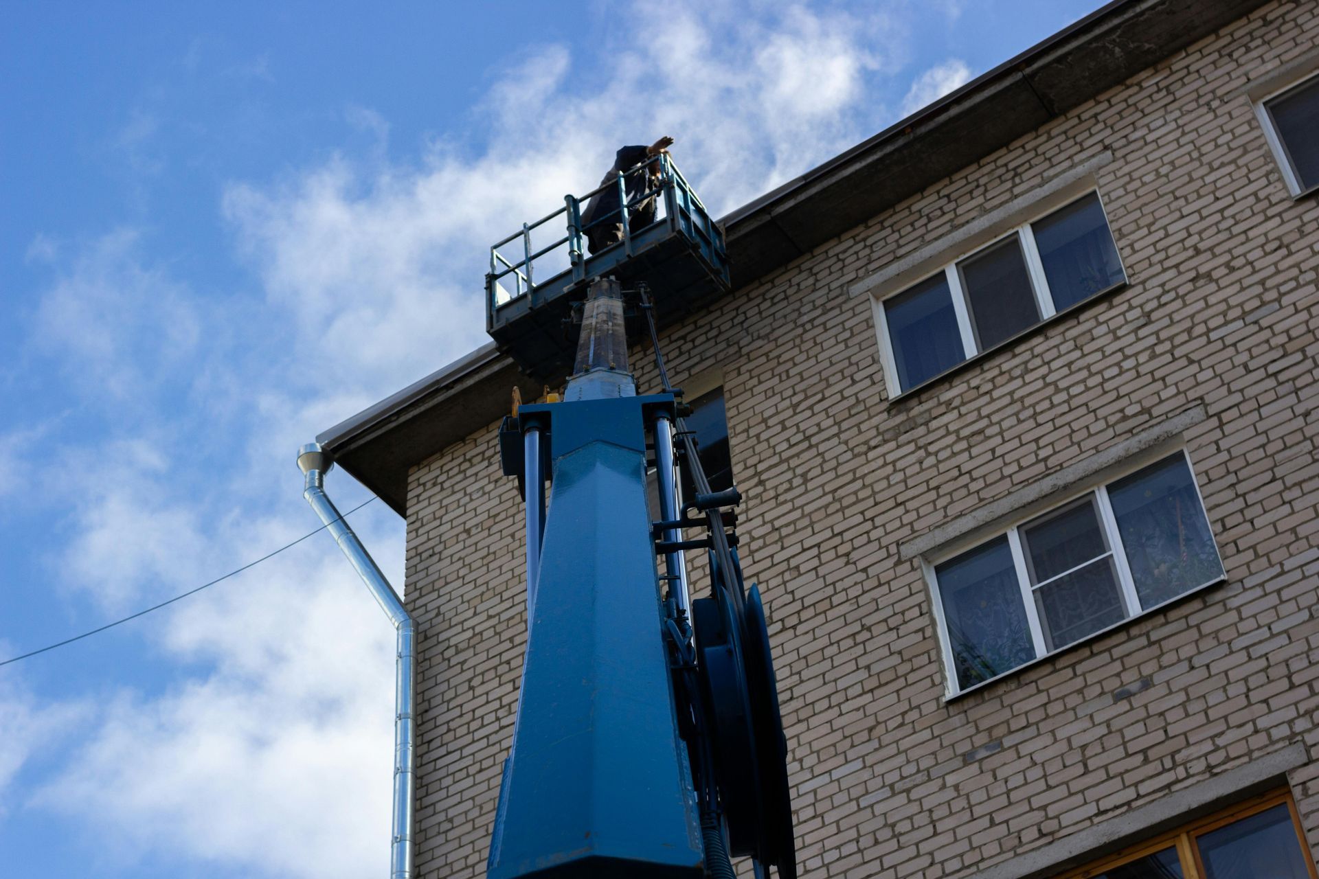 Blue cherry picker lifting workers beside a brick apartment building under a cloudy sky