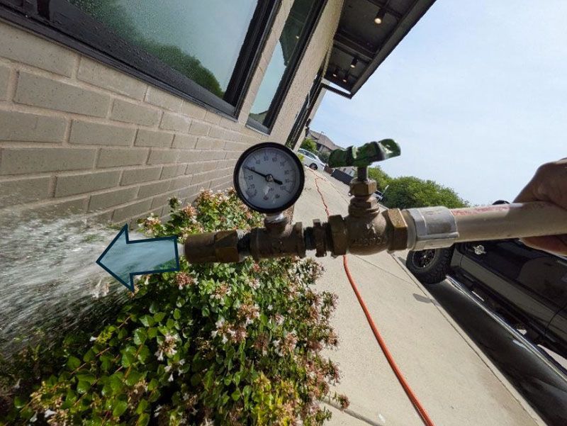 Calibrated spray nozzle performing AAMA 501.2 water testing at a San Antonio storefront.