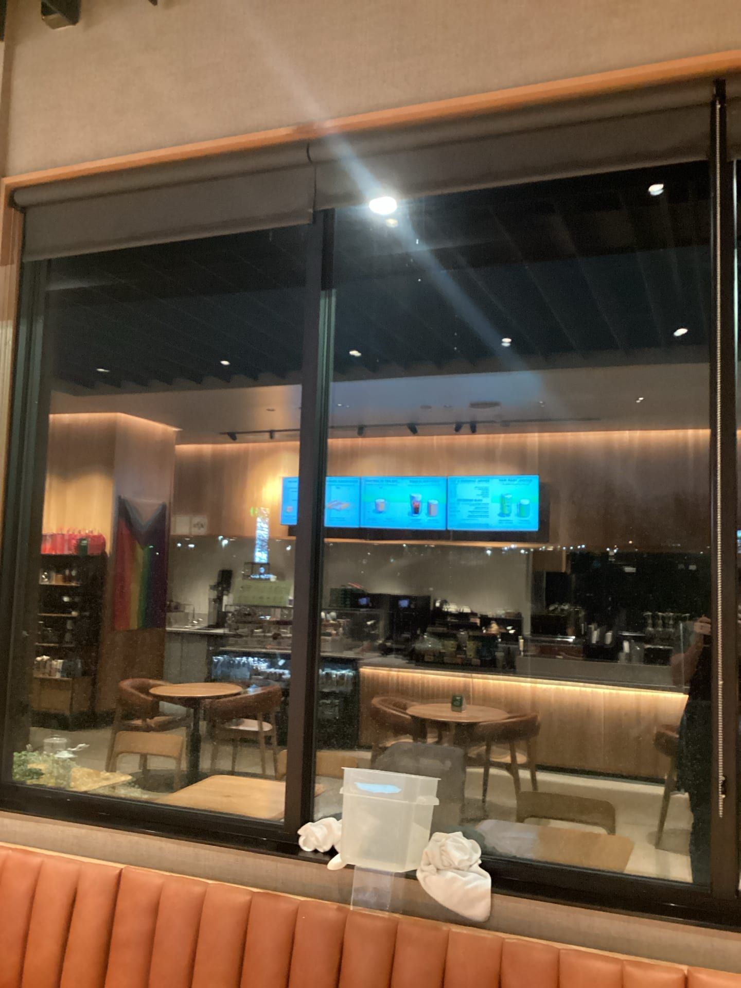 Modern restaurant interior seen through large window, with tables, stools, and blue-lit menu screens.