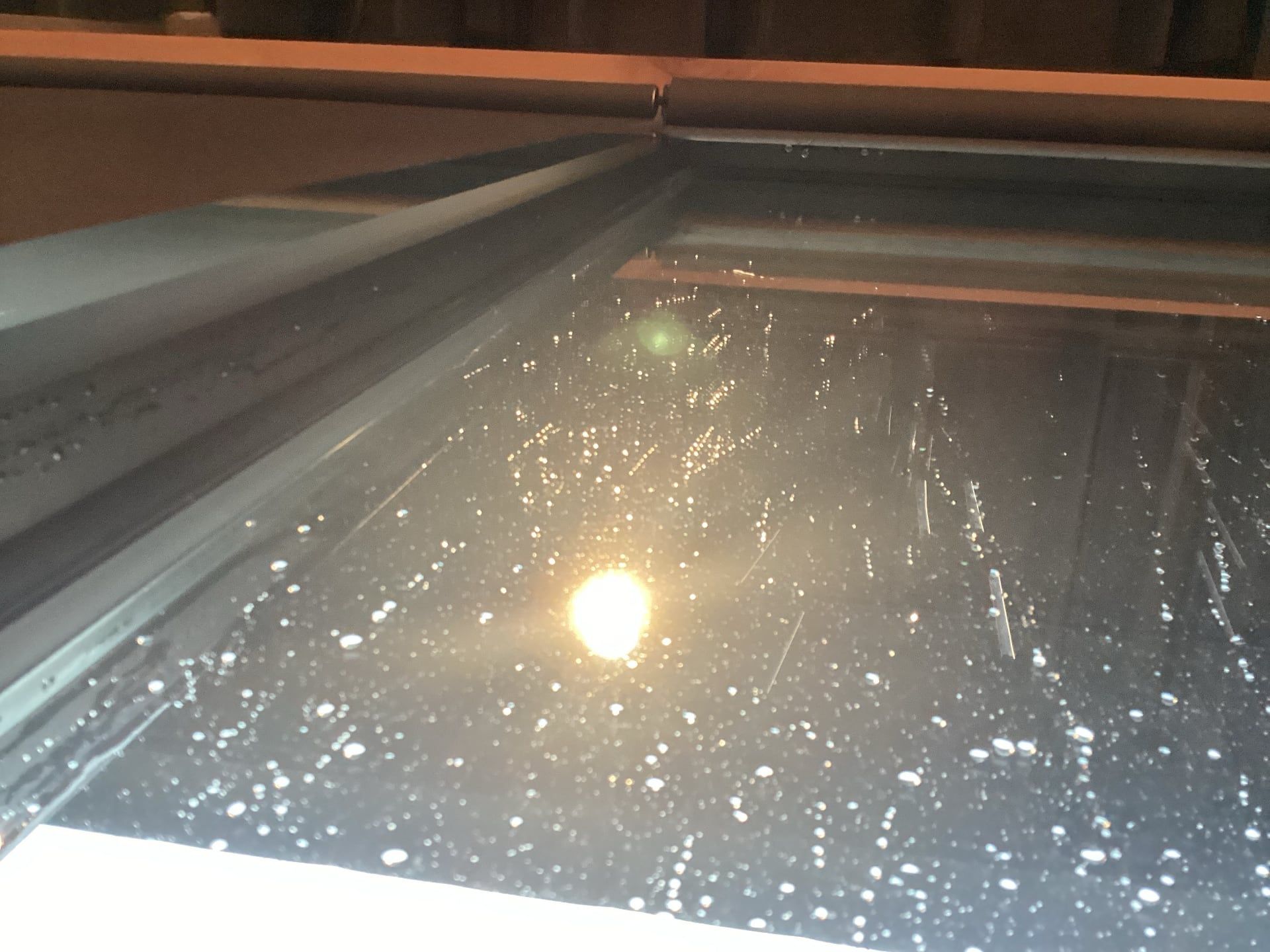 Rain-speckled window reflecting lights and a bright circular glare at night