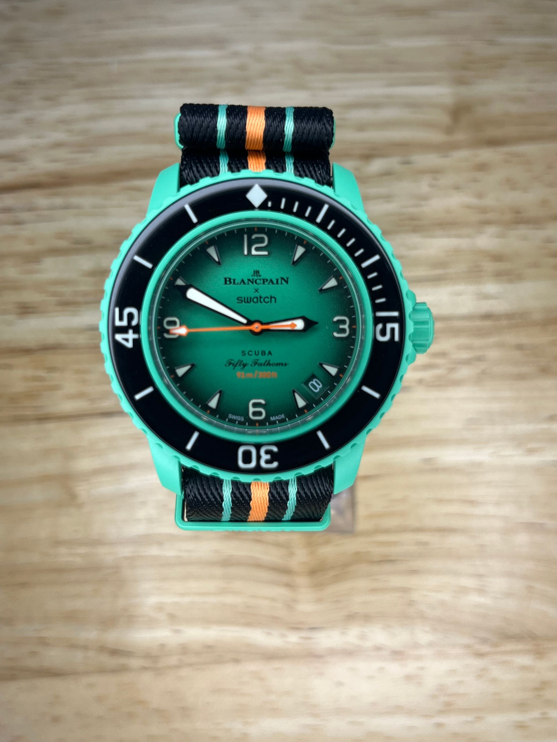Green wristwatch with black bezel and striped band, on a wood surface.