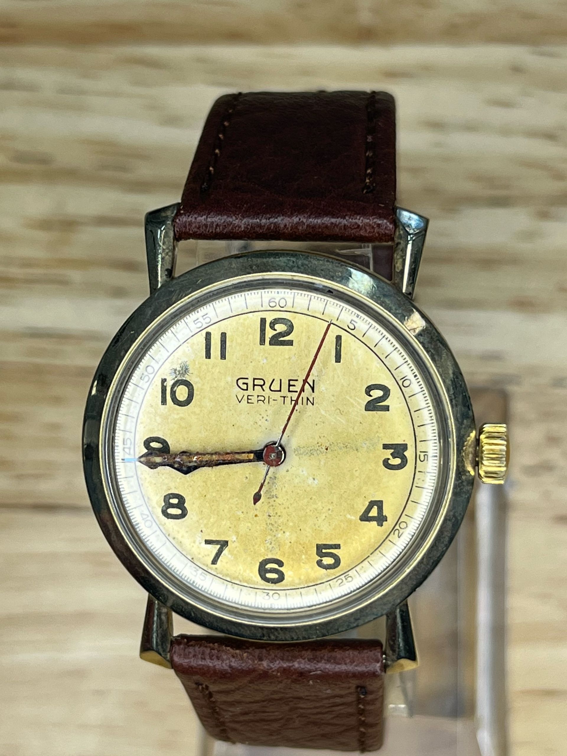 Vintage Gruen Veri-thin watch with a gold face, black numbers, and brown leather band.