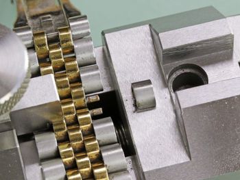 Watch bracelet being resized in a watch repair tool; silver metal, gold links, close-up view.