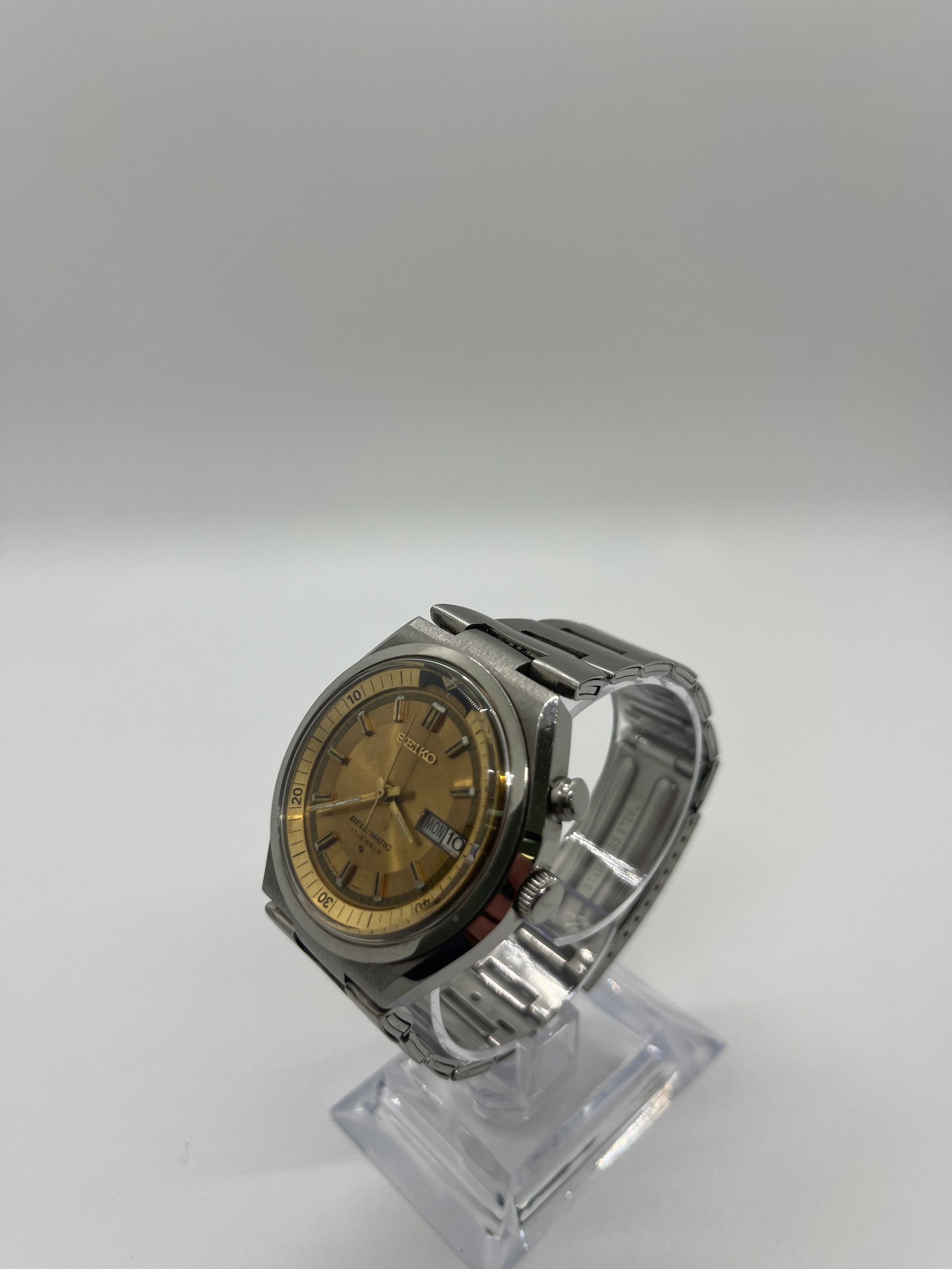 Silver wristwatch with gold face, on clear display stand.