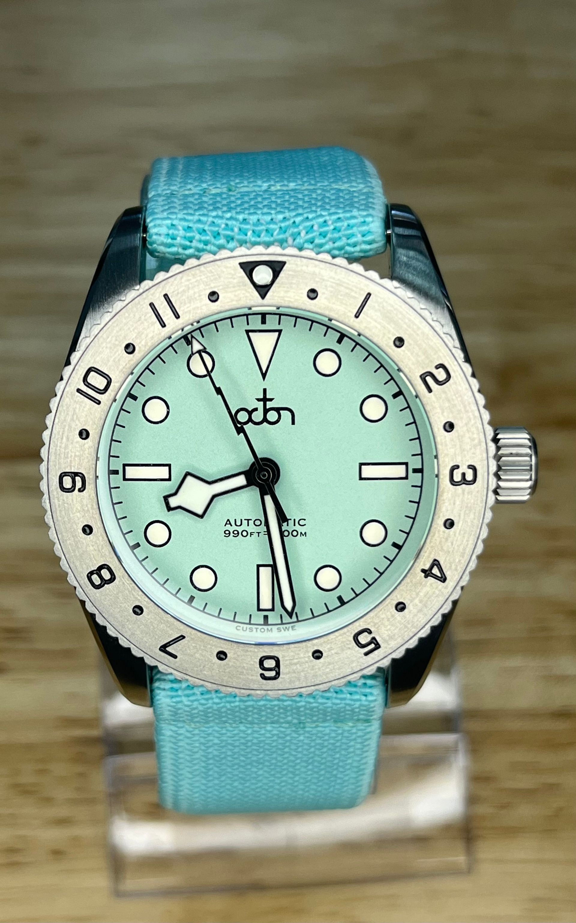 A light blue watch with a matching strap. The watch face is mint green, and the bezel is silver.