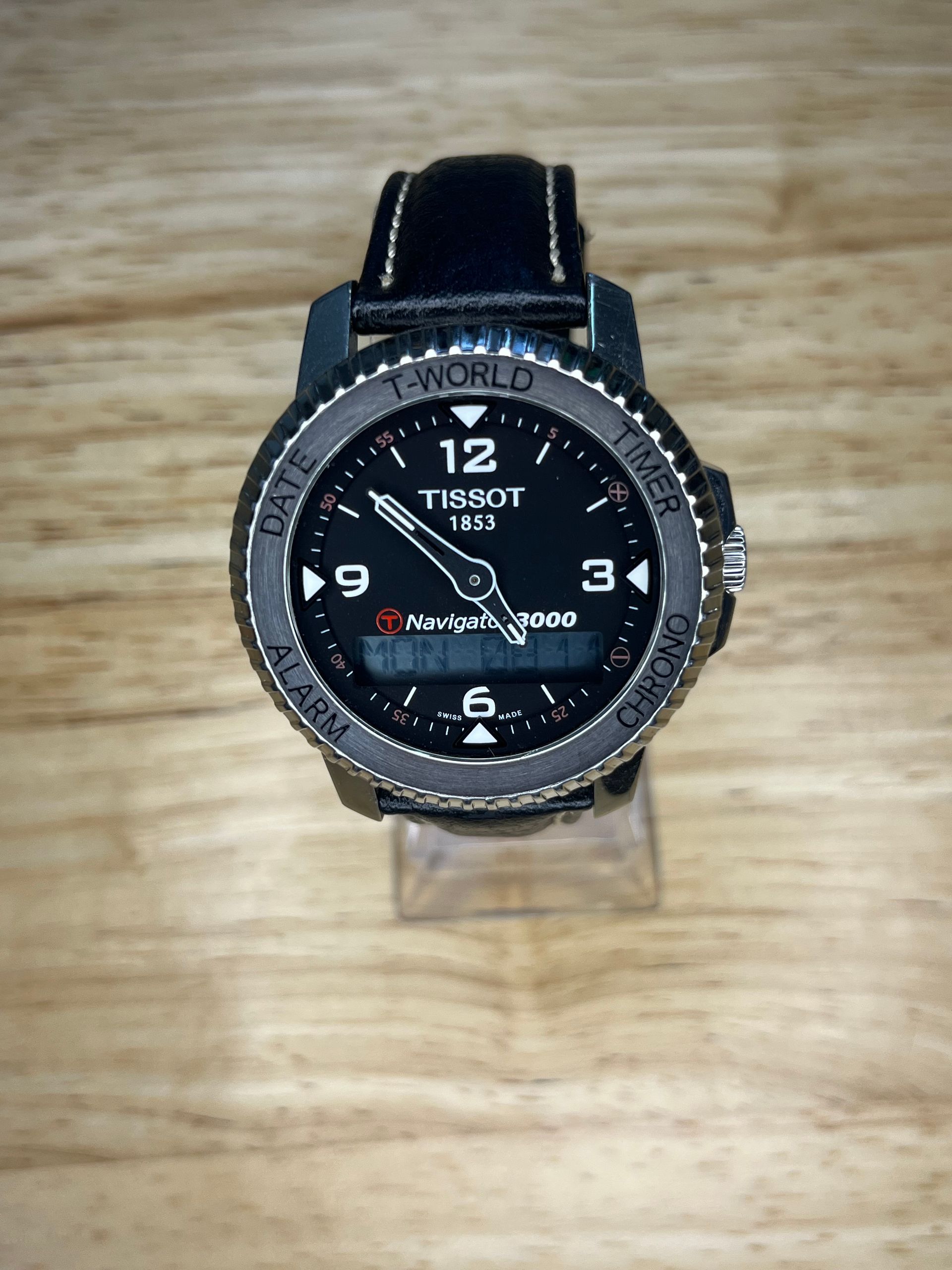 Black Tissot T-Touch watch with digital display and leather strap on wooden surface.