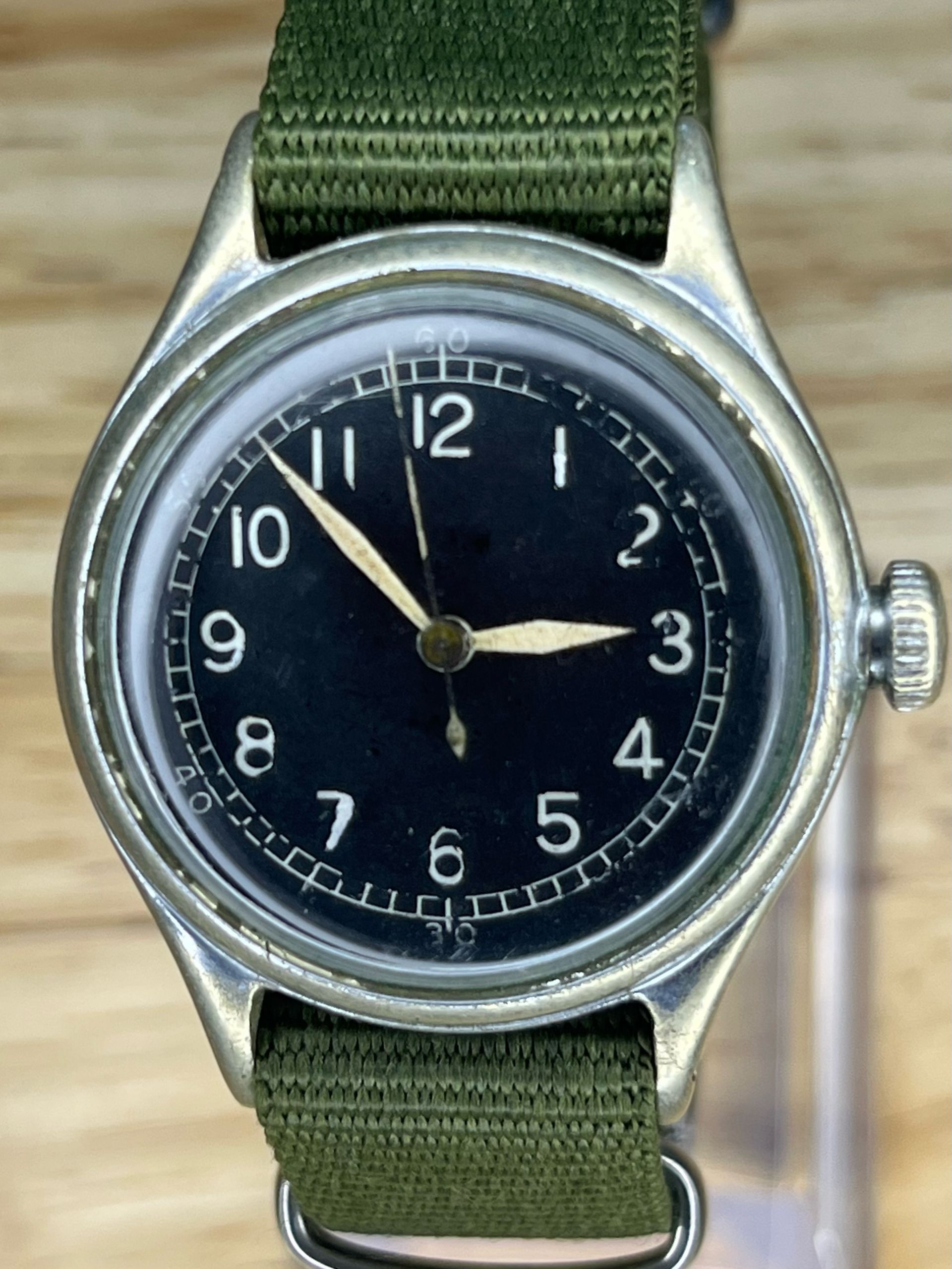 Vintage wristwatch with a black face, white numerals, and a green strap.
