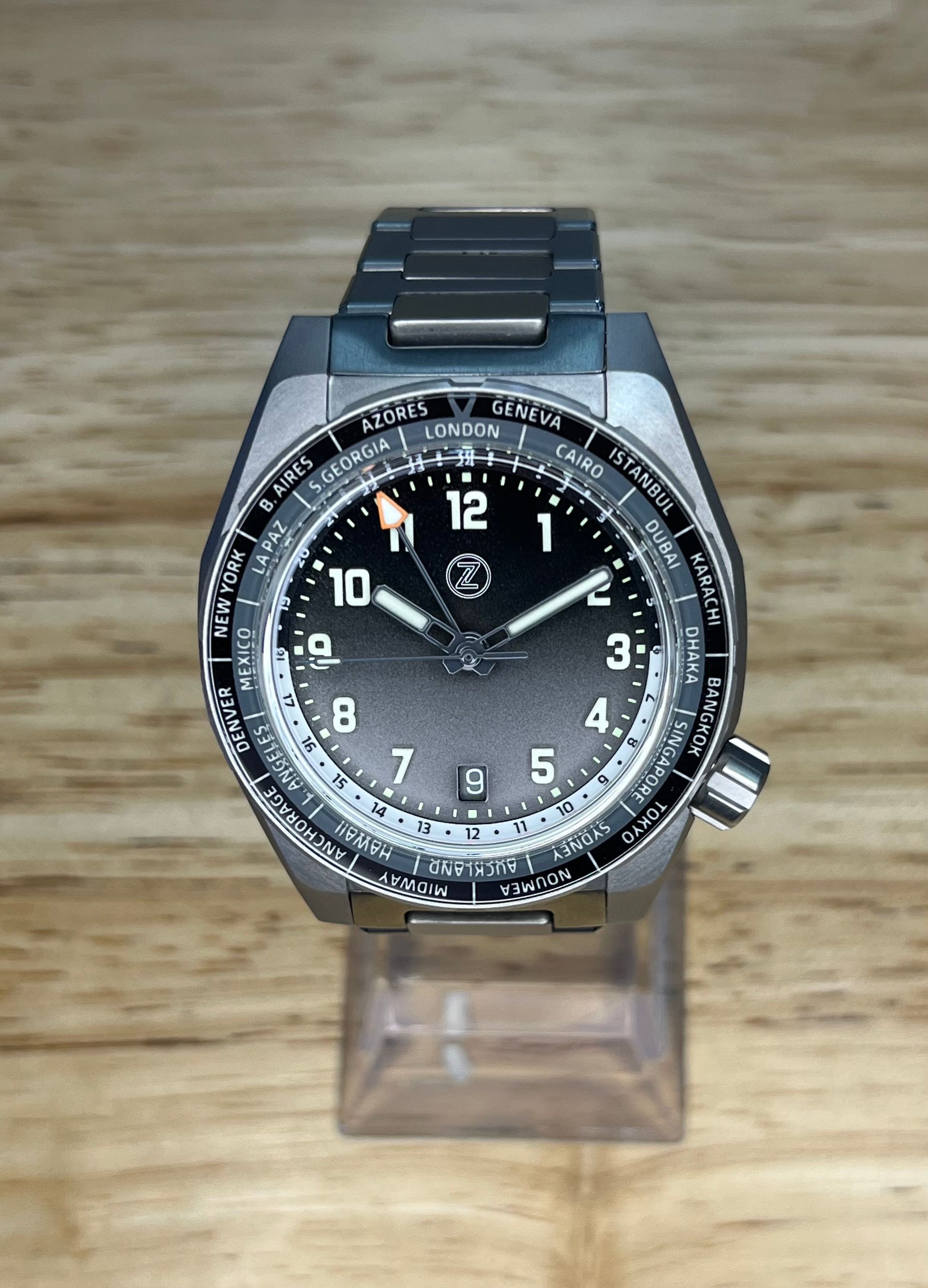 Titanium wristwatch with a black face and world time bezel on a wooden surface.