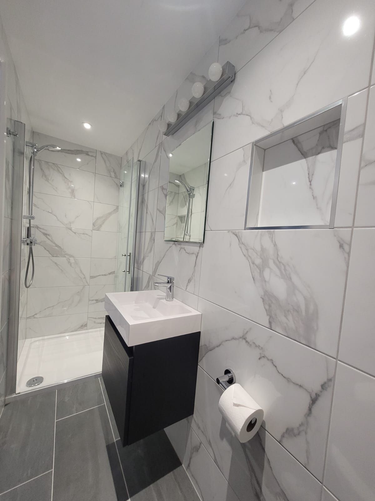 A bathroom with marble tiles , a sink , a mirror and a shower.