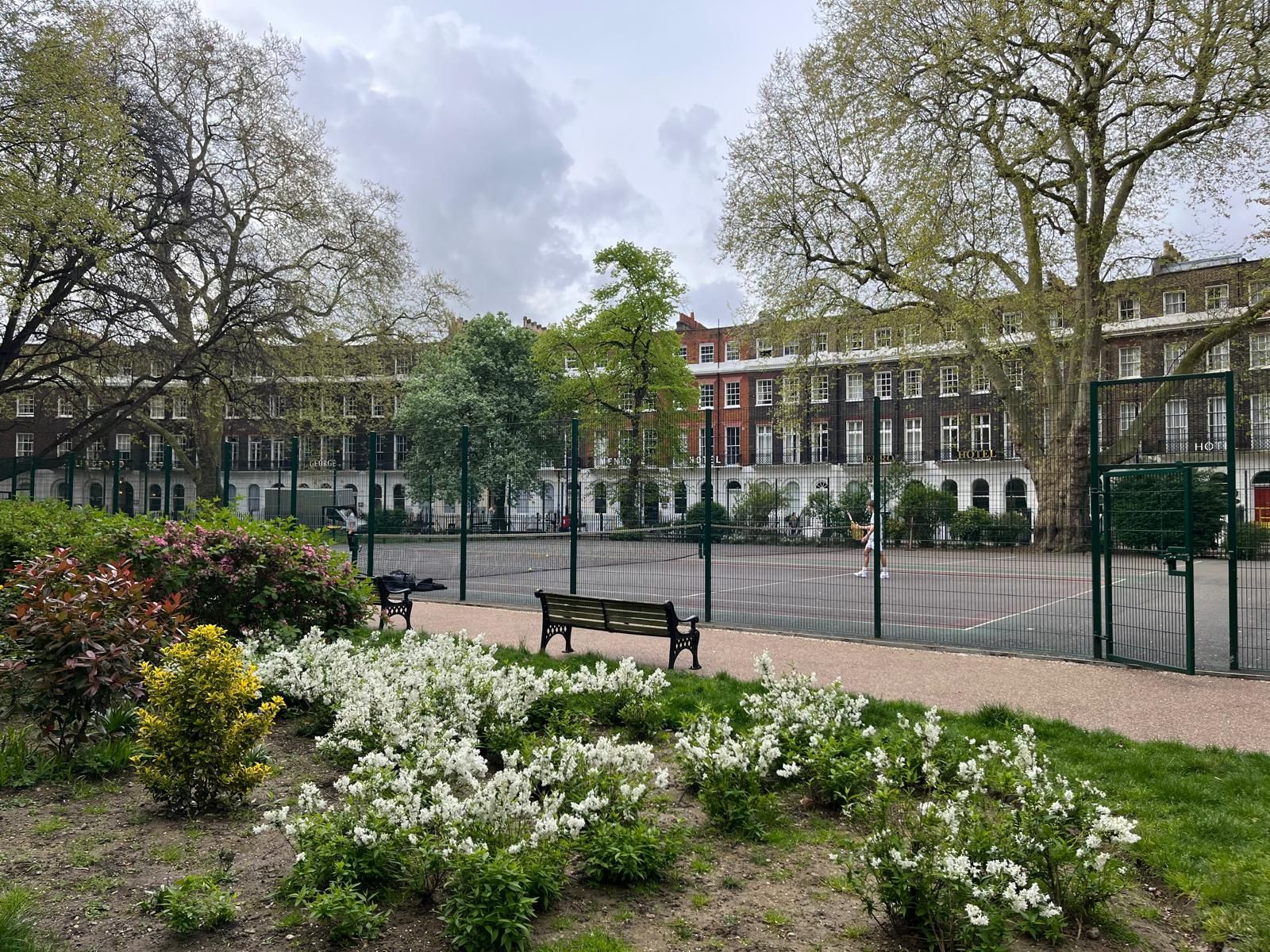 A park with a bench and flowers in front of a building.