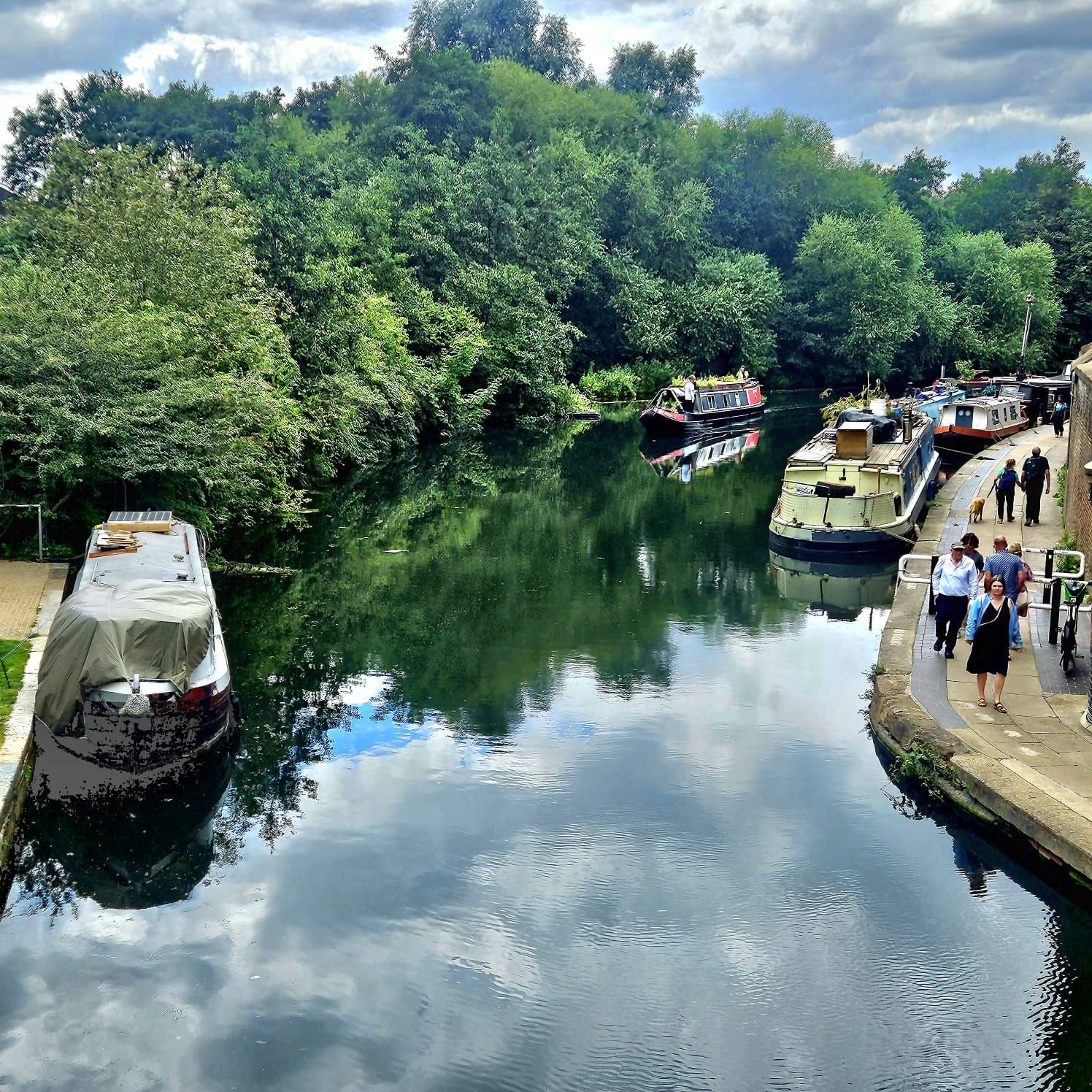 A group of people are walking along a river with boats in it