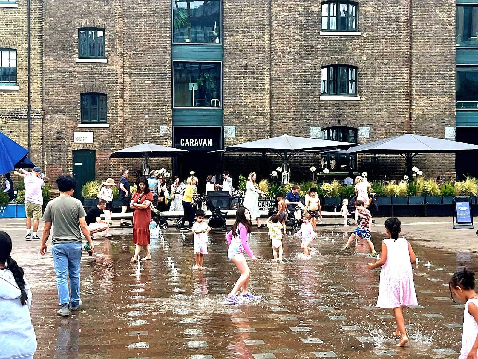A group of people are playing in a fountain in front of a building.
