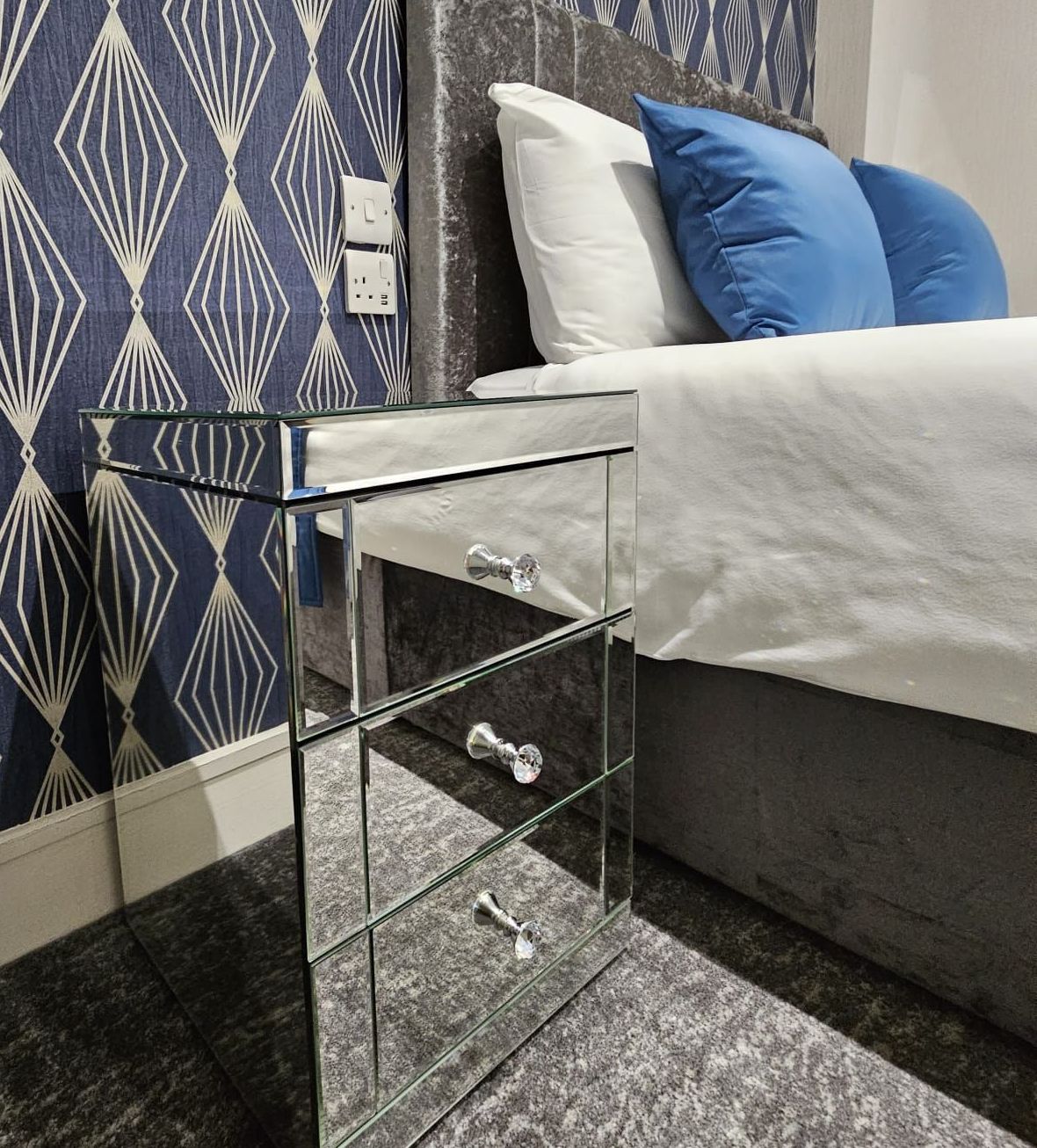 A bedroom with a bed and a mirrored nightstand