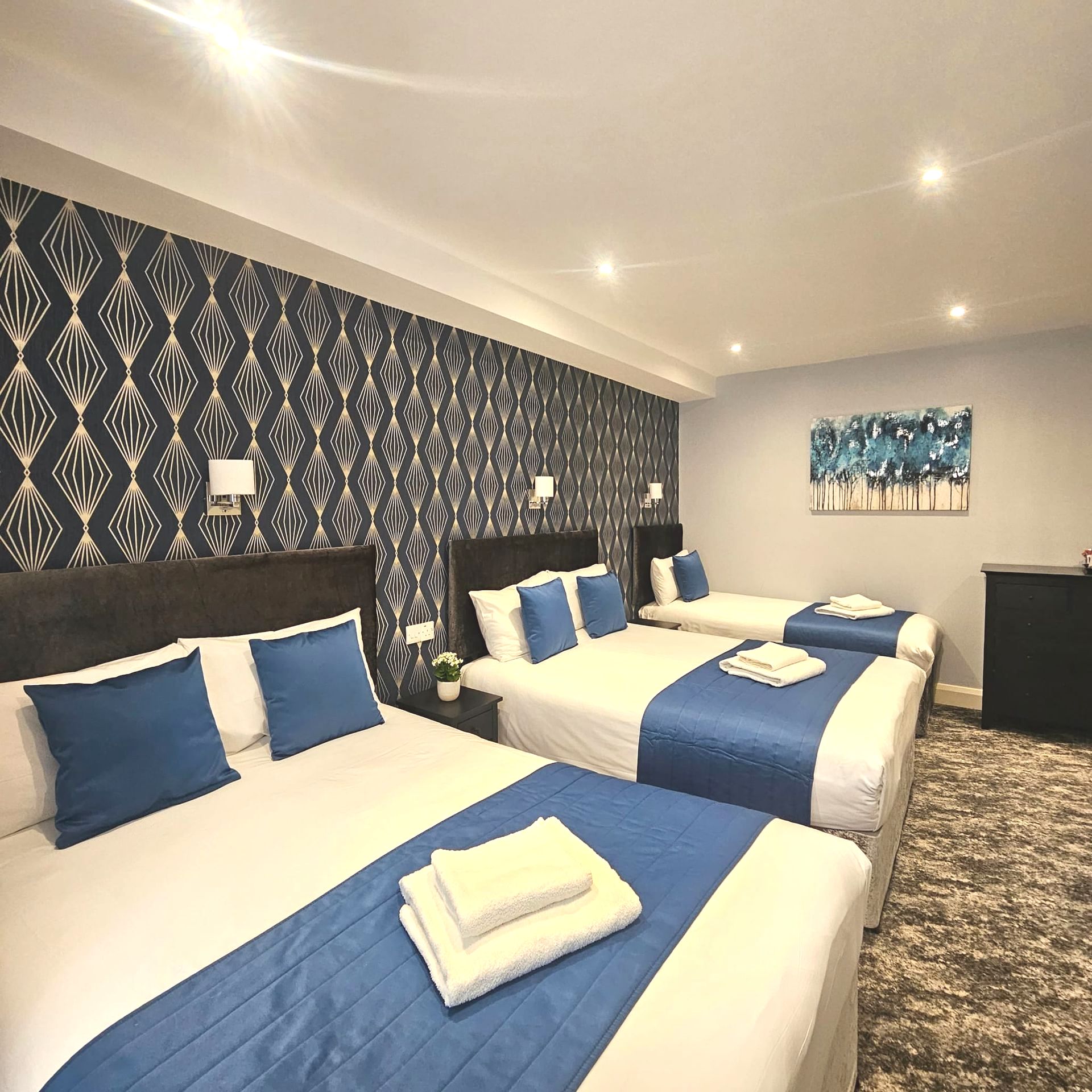 A hotel room with three beds and blue sheets