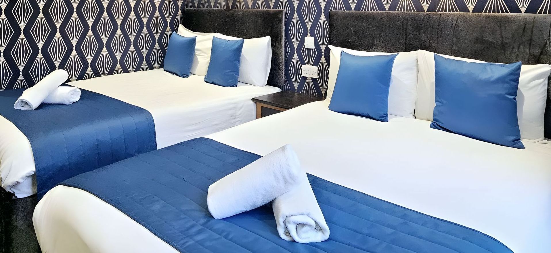 A hotel room with three beds and blue pillows.