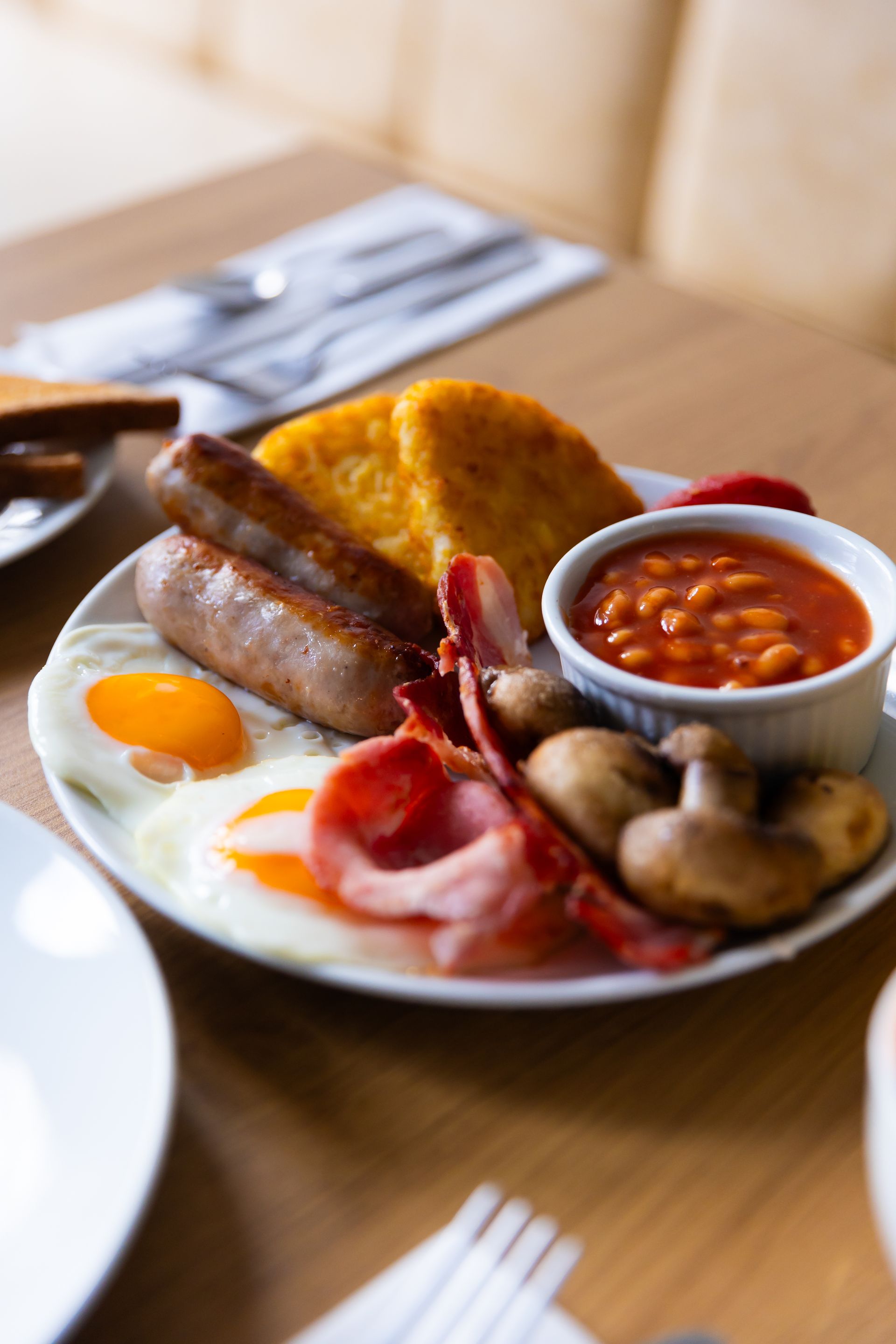 A plate of food with eggs , sausages , bacon , mushrooms and baked beans on a table.