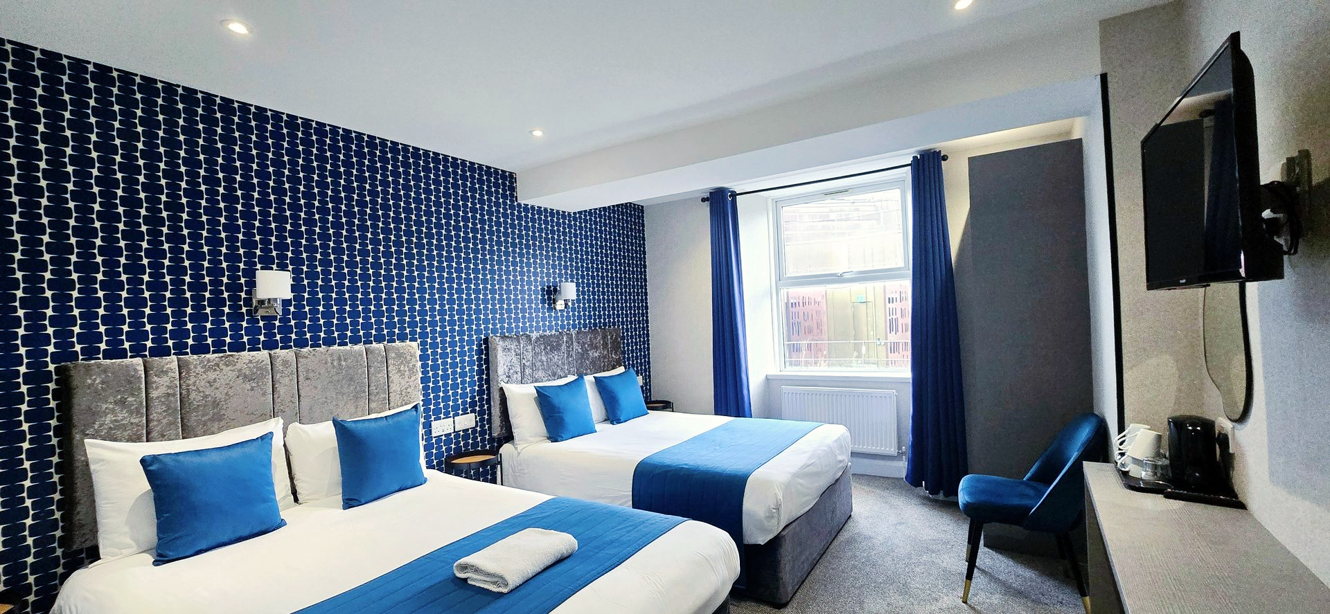 Hotel room with two double beds, blue and white decor, window and TV.
