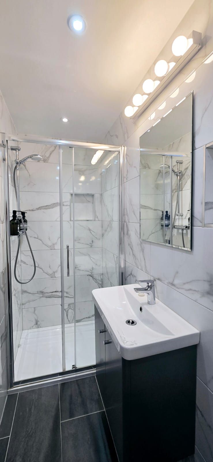 Bathroom with a white marble-look shower, vanity with a dark green cabinet, and a large mirror.