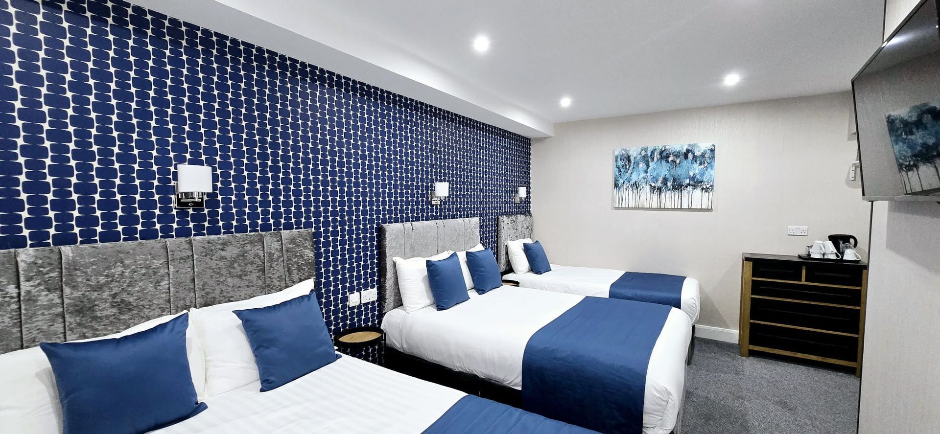 A hotel room with three beds and blue sheets