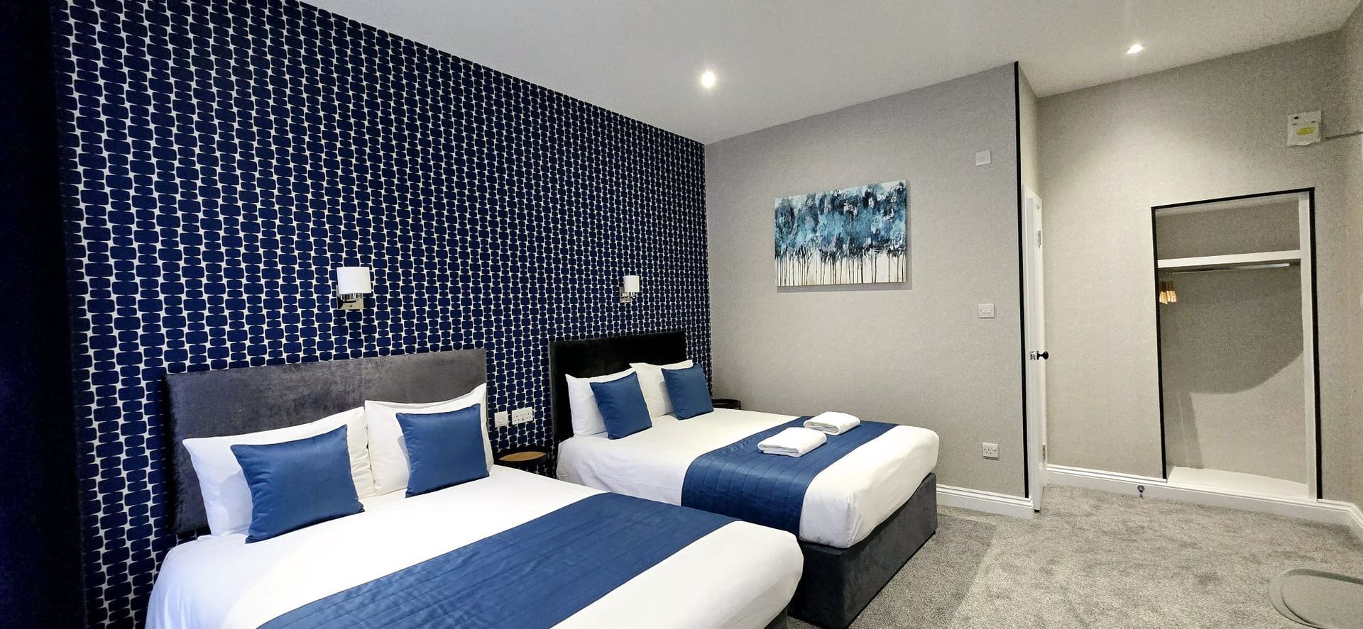 Modern hotel room with two double beds, patterned accent wall, and wall-mounted TV