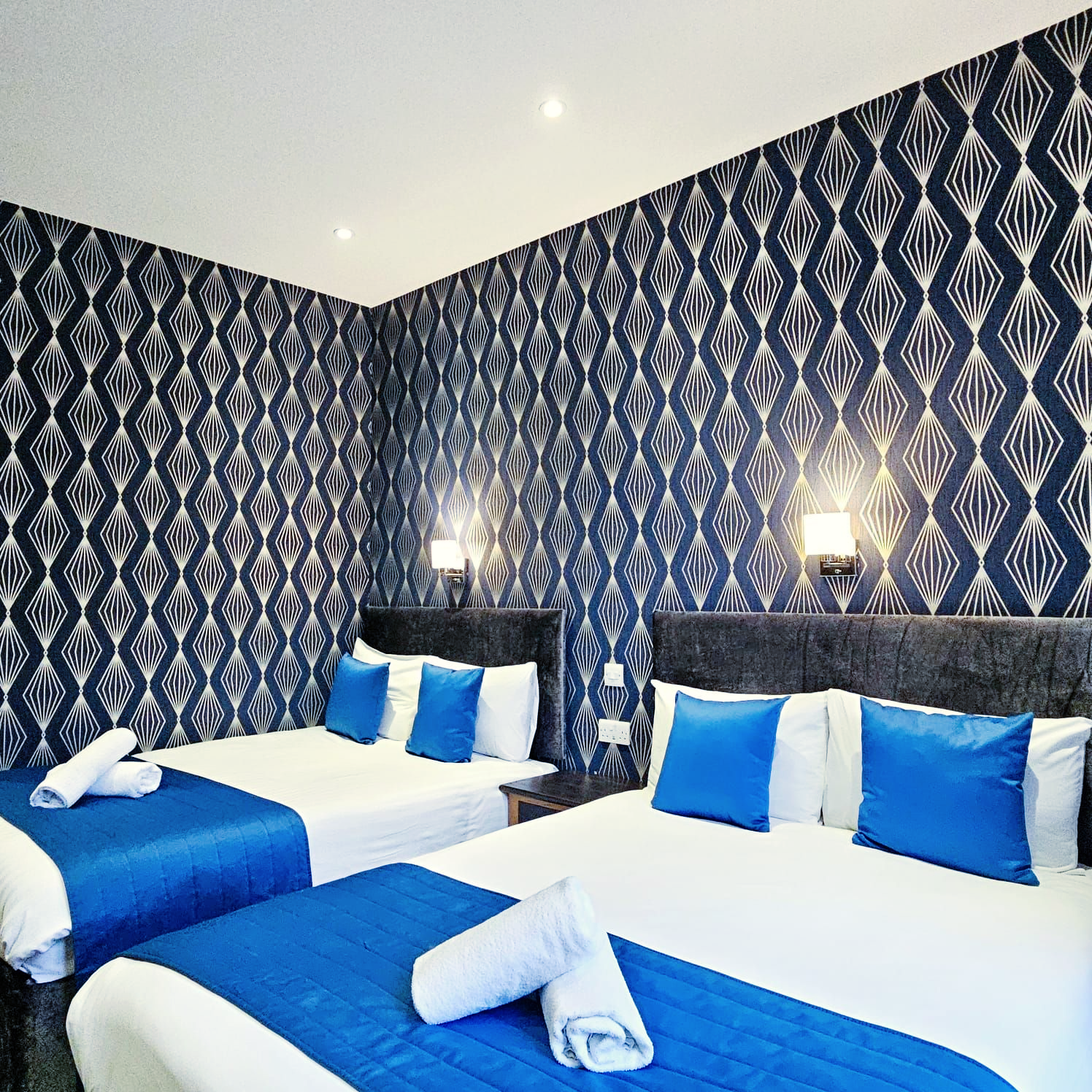 A hotel room with two beds and blue pillows