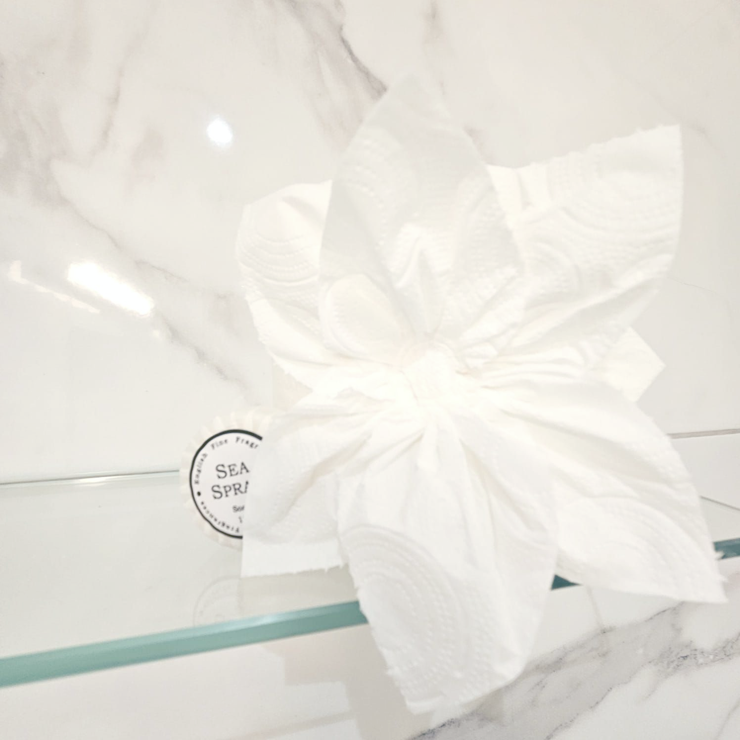A white flower is on a glass shelf next to a sea spa logo