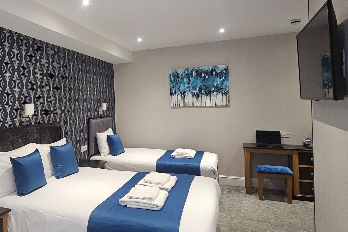 A hotel room with two beds , a desk and a flat screen tv.
