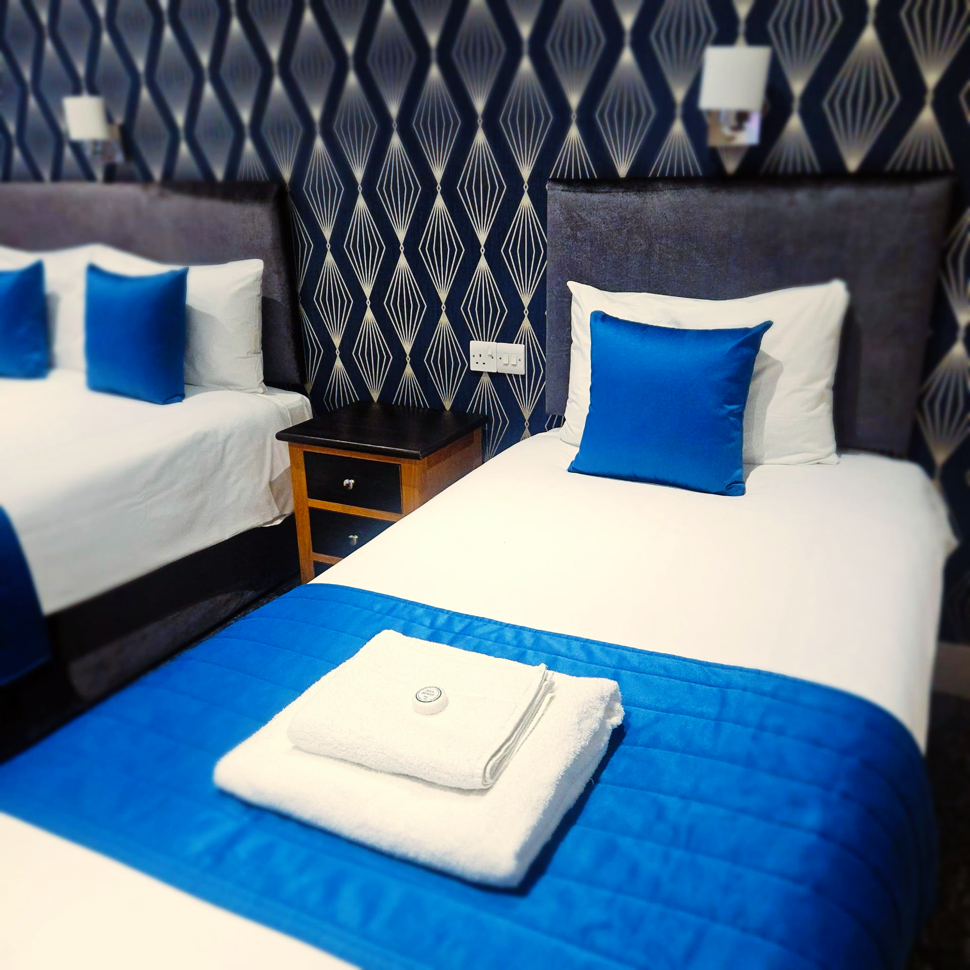 A hotel room with two beds and blue pillows