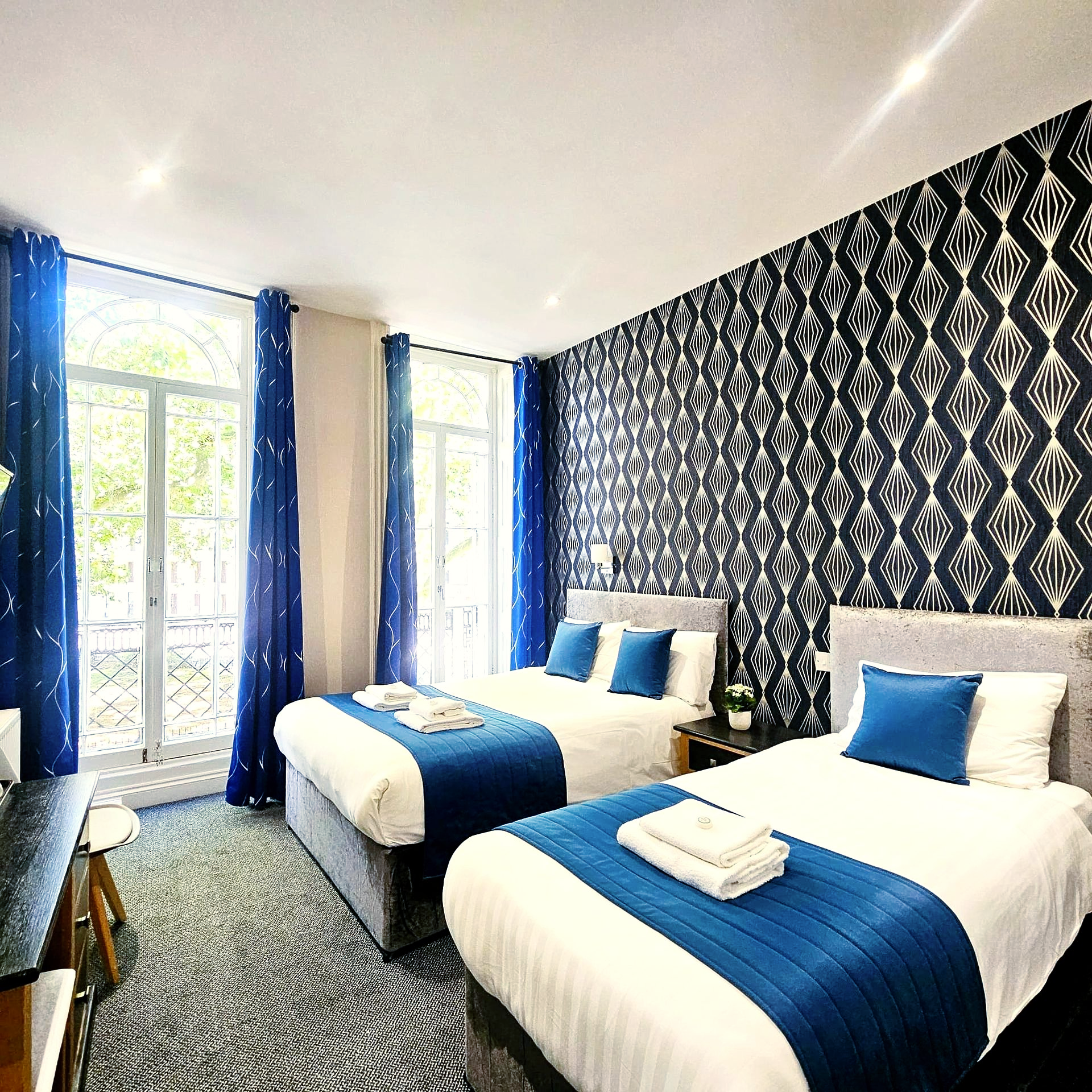 A hotel room with two beds and blue curtains