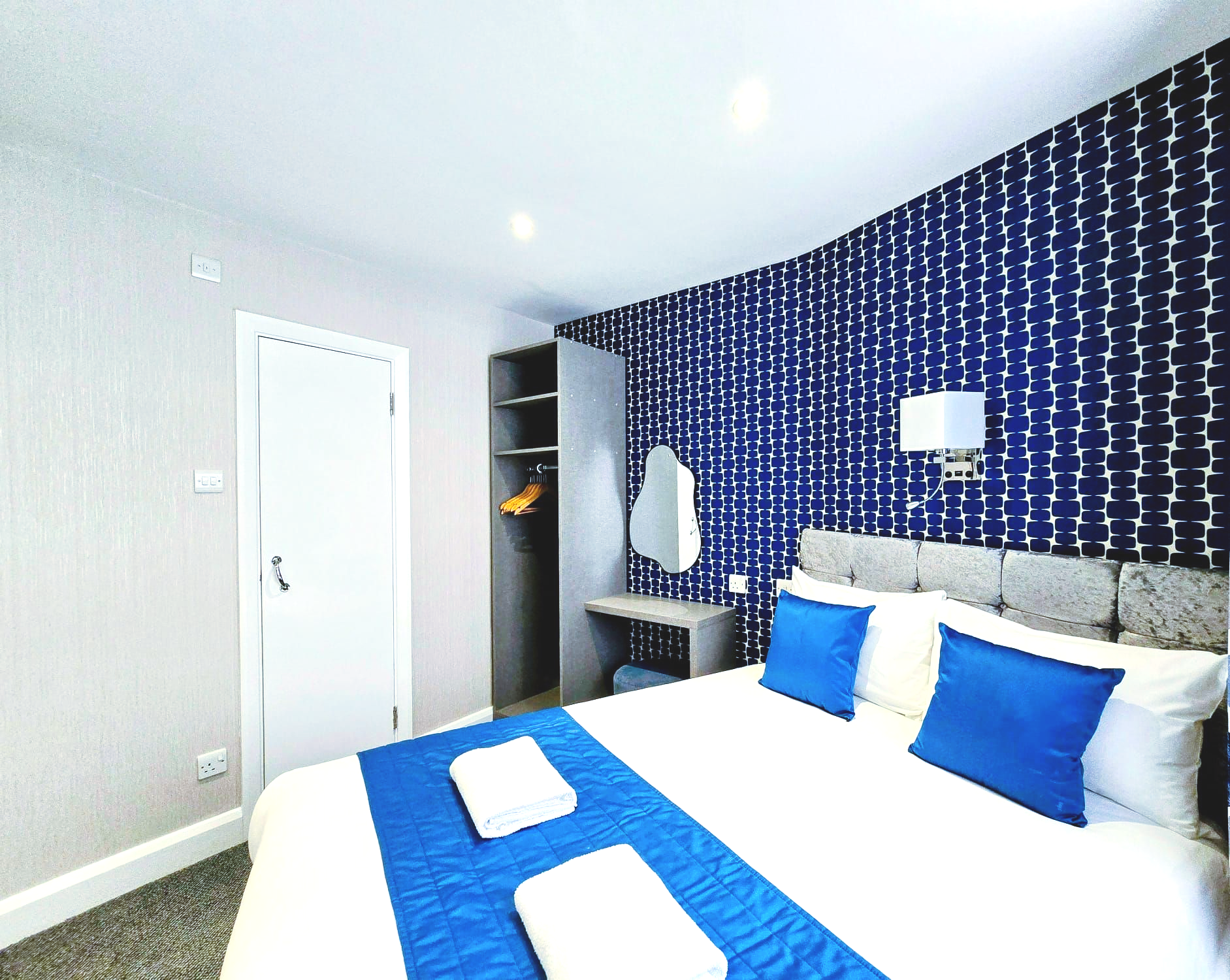 A hotel room with a king size bed and blue and white pillows.