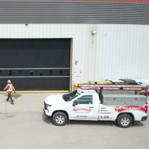 Warehouse exterior with open loading bay, worker on forklift, and white pickup truck in front