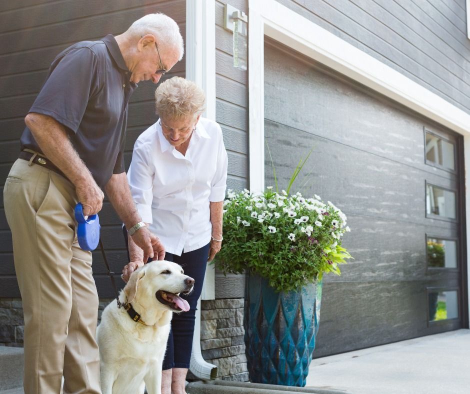 Older couple standing by a front door with a dog beside a large blue planter.