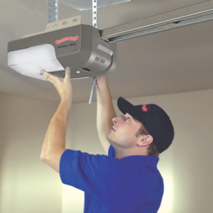 Man in blue shirt and cap adjusting a garage door opener mounted to the ceiling