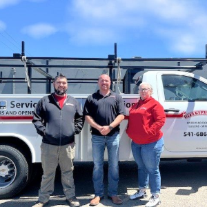 Three people standing beside a white service truck on a sunny street.