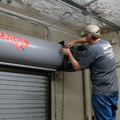 Worker installing a gray metal roll-up door in an industrial space
