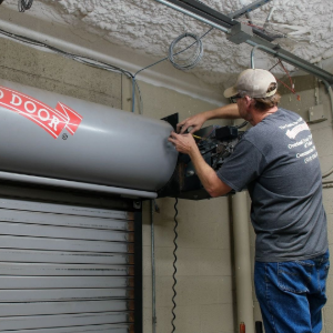 Worker installing a gray metal roll-up door in an industrial space
