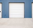 Blue warehouse wall with a white roll-up garage door and concrete driveway