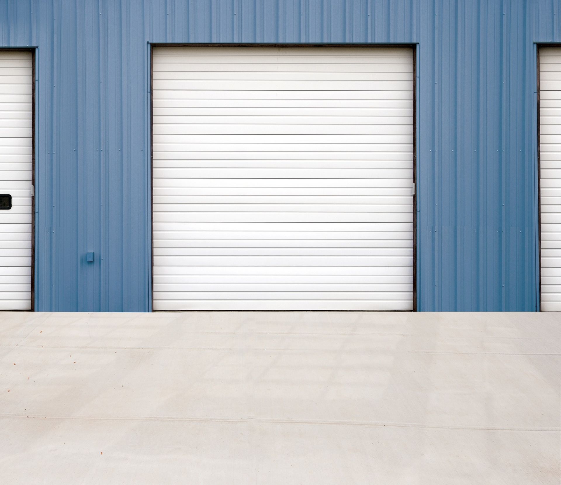 Blue warehouse wall with a white roll-up garage door and concrete driveway