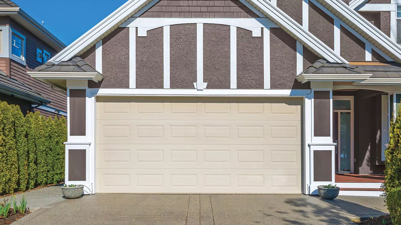 Front view of a beige two-car garage with white trim and a brick house exterior