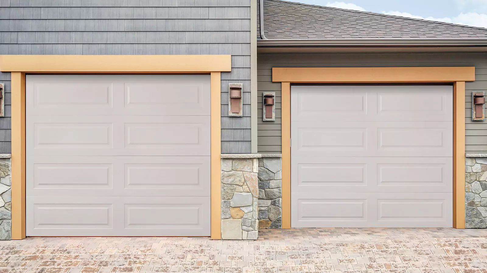 Side-by-side gray garage doors with tan trim on a stone-and-gray house exterior