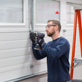 Man using a drill to install a garage door panel beside an orange ladder