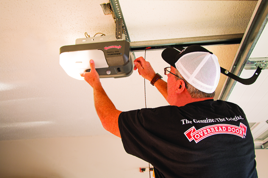 Technician installing a garage door opener on the ceiling with a tool.