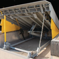 Industrial dock leveler with raised metal platform and yellow support arms at a loading bay