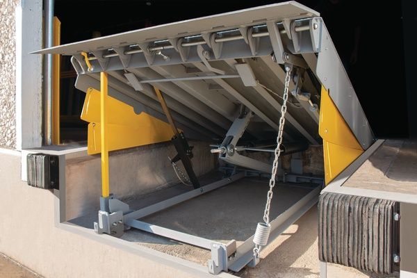 Raised metal loading dock ramp with yellow supports and chains in a warehouse doorway
