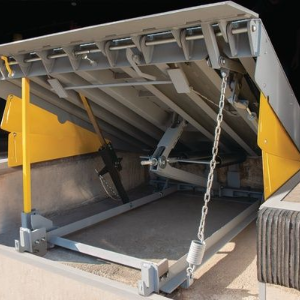 Industrial dock leveler with raised metal platform and yellow support arms at a loading bay